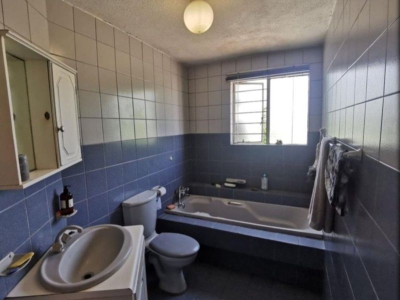 A dated bathroom featuring a built-in bathtub, wall-mounted vanity, and blue and white ceramic wall tiling throughout.