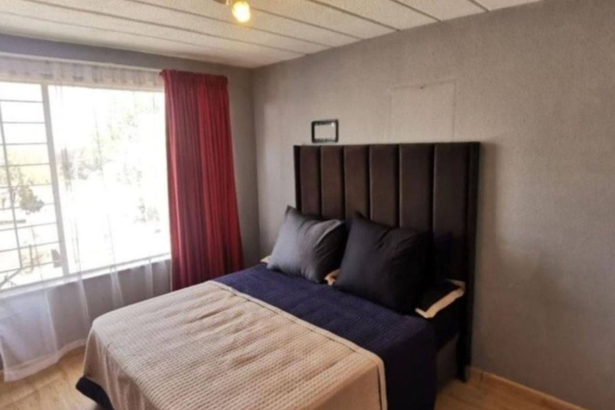 A functional bedroom featuring laminate flooring, a large window for natural light, and a textured ceiling finish.