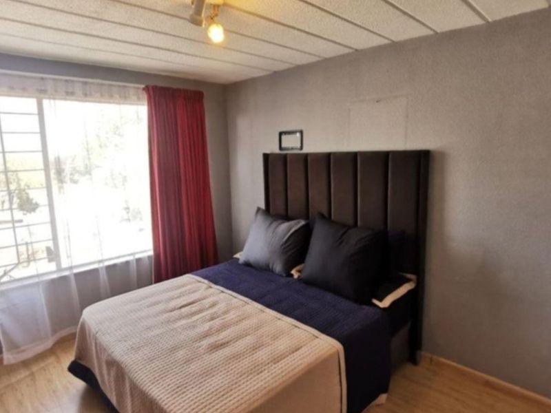 A functional bedroom featuring laminate flooring, a large window for natural light, and a textured ceiling finish.