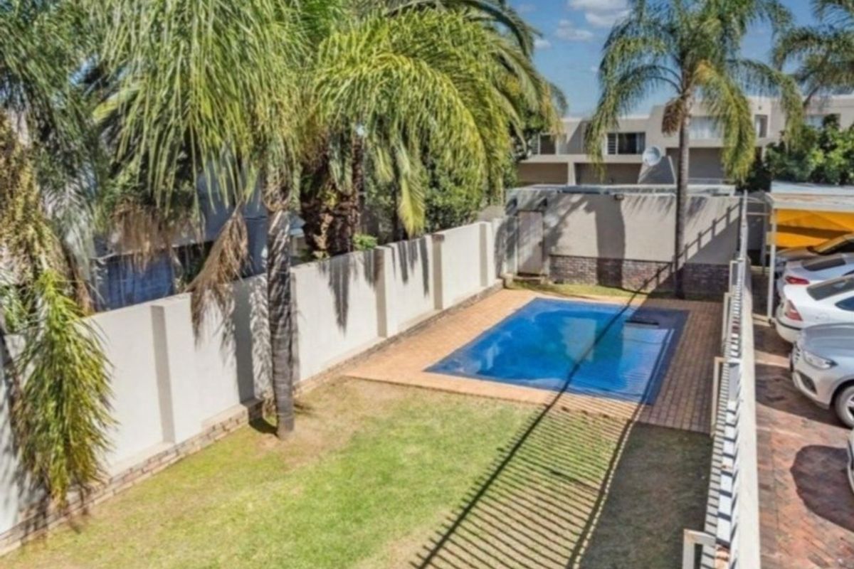 Outdoor area featuring a swimming pool with paved surround, lawn, and perimeter walling, providing a private space within the apartment complex grounds.