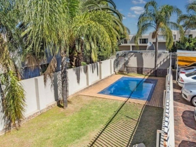 Outdoor area featuring a swimming pool with paved surround, lawn, and perimeter walling, providing a private space within the apartment complex grounds.