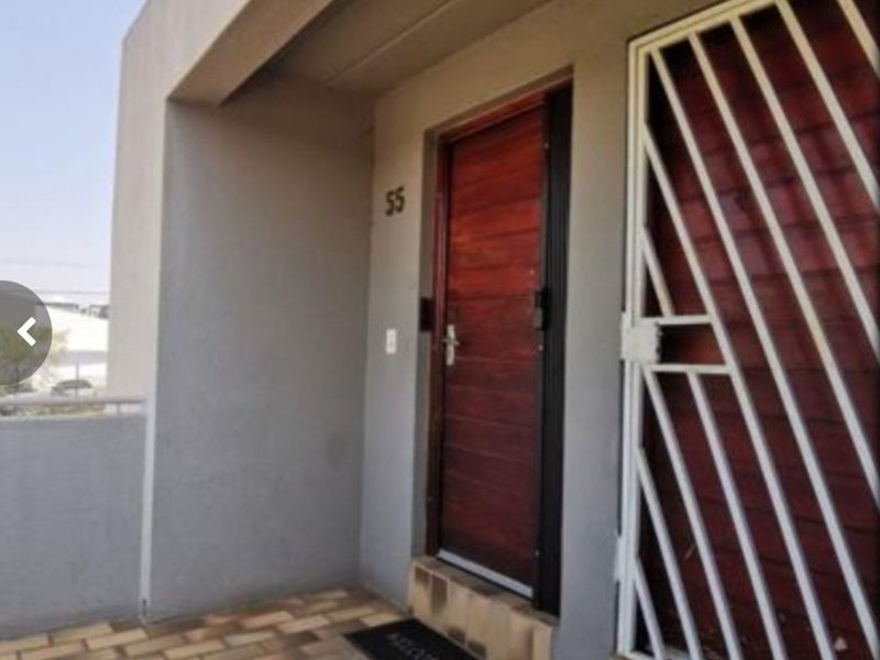 A private apartment entrance featuring a solid timber front door and a white metal security gate on a paved landing.