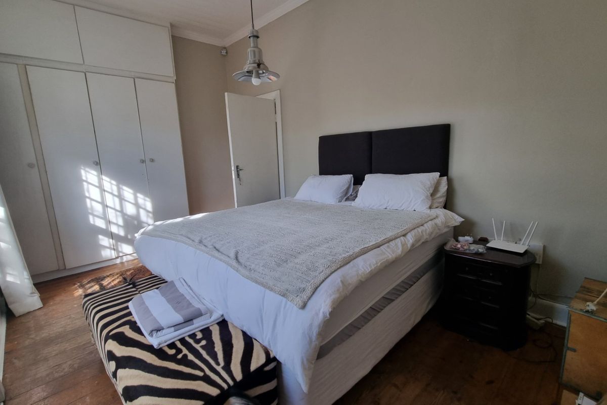 A bedroom featuring hardwood flooring, built-in cupboards, and a neutral wall finish, offering a functional and well-lit living space.