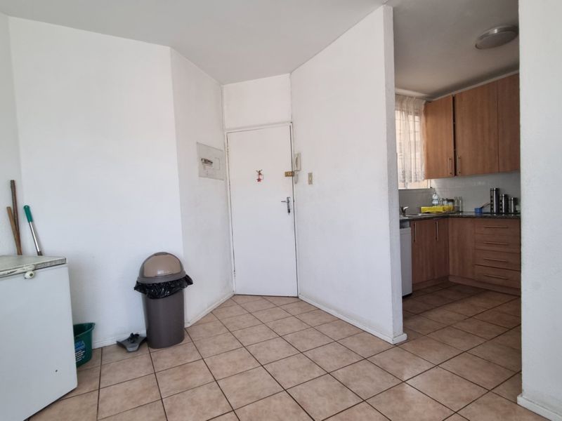 A functional kitchen area featuring tiled flooring, built-in wooden cabinetry, and a sink, with an adjacent entryway space.