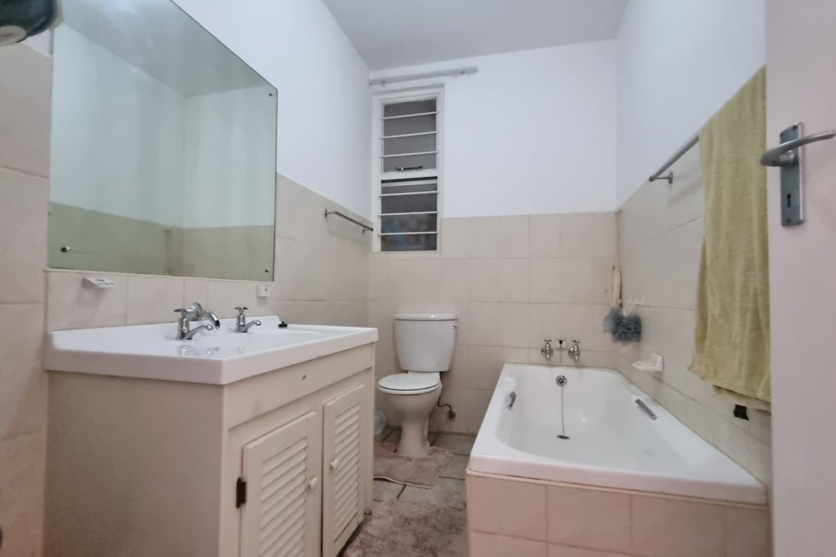 A functional bathroom featuring a vanity with basin, a standard bathtub, toilet, and tiled finishes, offering a dated but practical layout.