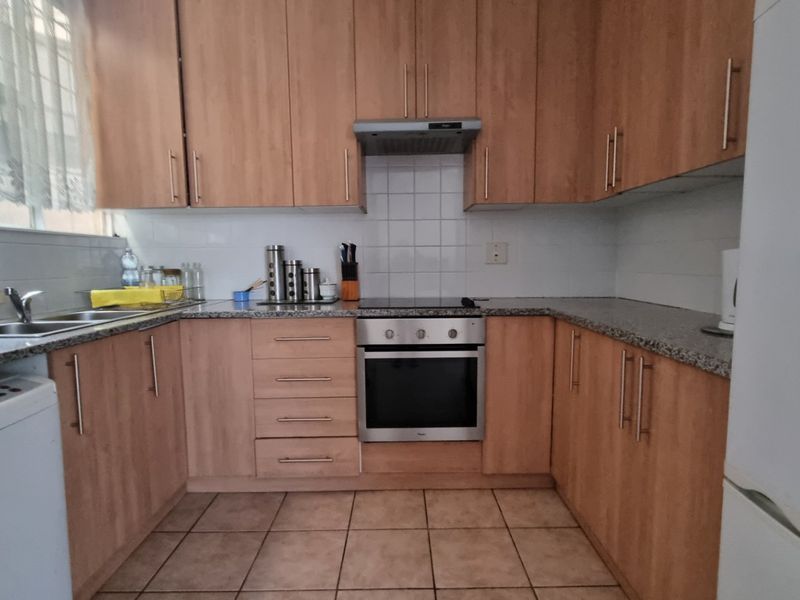 A functional U-shaped kitchen featuring light wood-finish cabinetry, granite countertops, a built-in oven with hob, and tiled flooring.