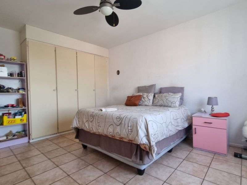 A bedroom featuring tiled flooring, a ceiling fan, and built-in cupboards, offering a functional space with potential for cosmetic updates.