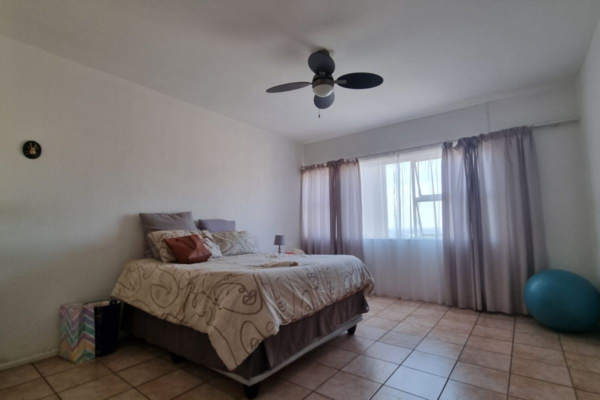 A spacious bedroom featuring tiled flooring, a ceiling fan, and a large window that allows for natural light.
