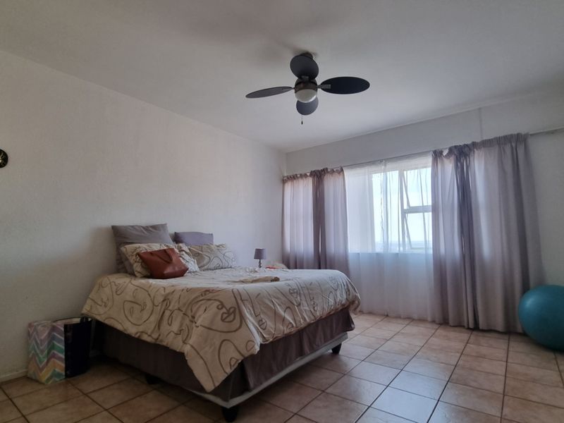 A spacious bedroom featuring tiled flooring, a ceiling fan, and a large window that allows for natural light.