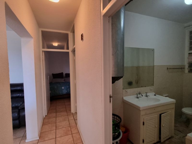 A view from the hallway looking into a bathroom and adjacent bedroom, featuring tiled flooring and dated bathroom fixtures.