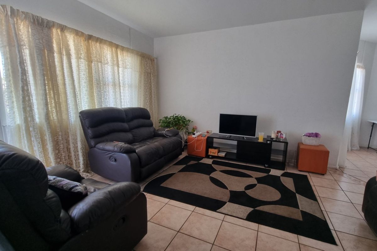 A living room featuring tiled flooring and a large window with natural light, providing a functional and neutral space for relaxation.