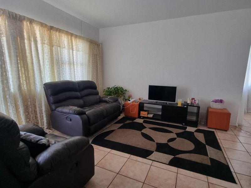 A living room featuring tiled flooring and a large window with natural light, providing a functional and neutral space for relaxation.