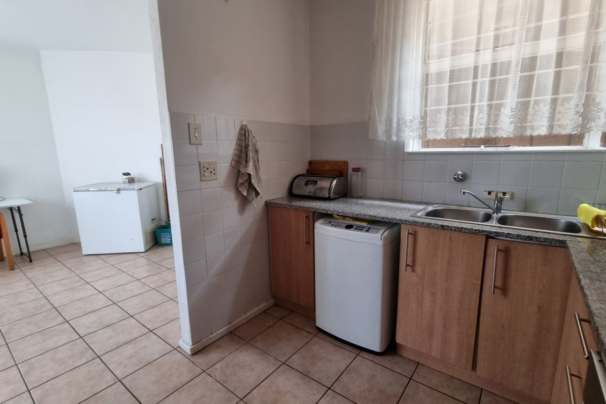 A functional kitchen area featuring laminate cabinetry, granite countertops, and a double bowl stainless steel sink with tiled splashbacks and flooring.