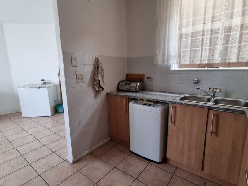 A functional kitchen area featuring laminate cabinetry, granite countertops, and a double bowl stainless steel sink with tiled splashbacks and flooring.