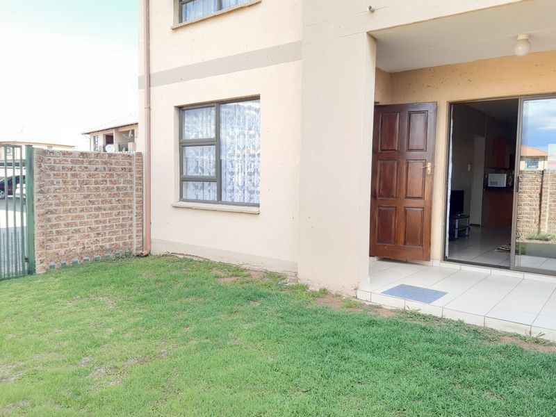 Rear view of the apartment featuring a small private garden, a tiled patio area, and direct access through a sliding glass door.