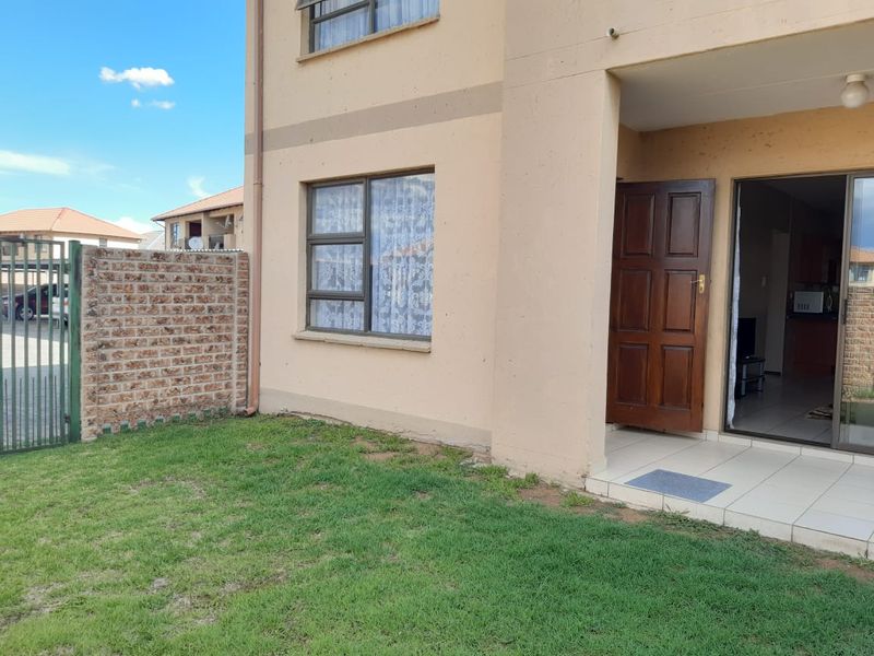 Exterior view of an apartment unit featuring a small private garden, brick boundary wall, tiled patio entrance, and aluminium window frames.