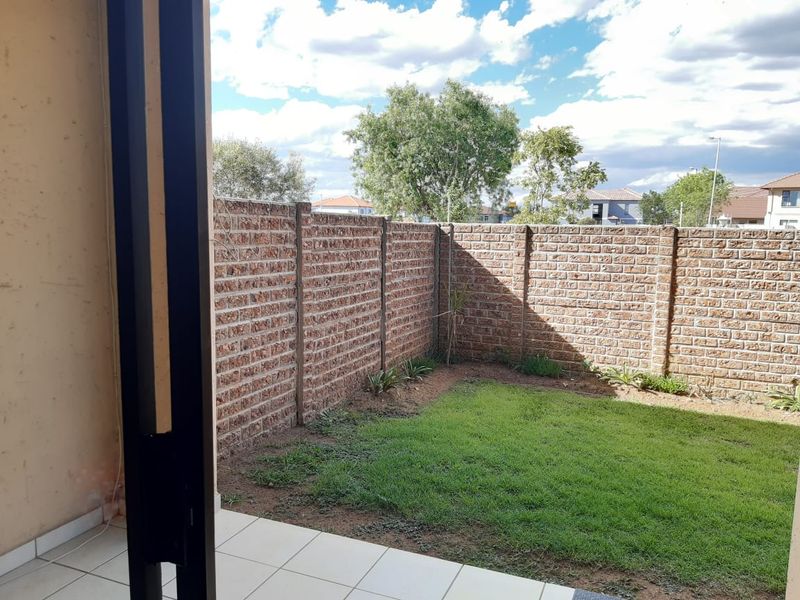 A private rear garden featuring a small lawn area, tiled patio, and secure brick boundary walls.