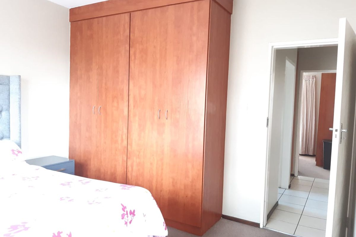 A bedroom featuring a large built-in wooden wardrobe, carpeted flooring, and an open doorway leading to a tiled hallway.