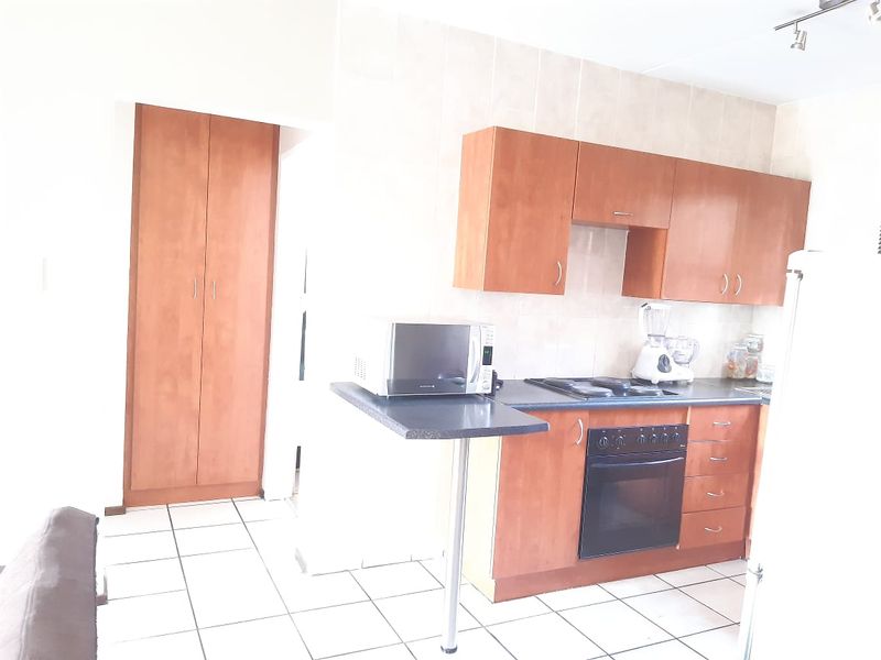 A functional kitchen featuring wooden cabinetry, dark laminate countertops, built-in oven and hob, tiled backsplash, and a convenient built-in pantry cupboard.