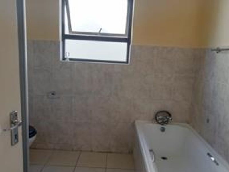 A functional bathroom featuring tiled walls and flooring, a standard bathtub, and a top-hung window for natural ventilation.