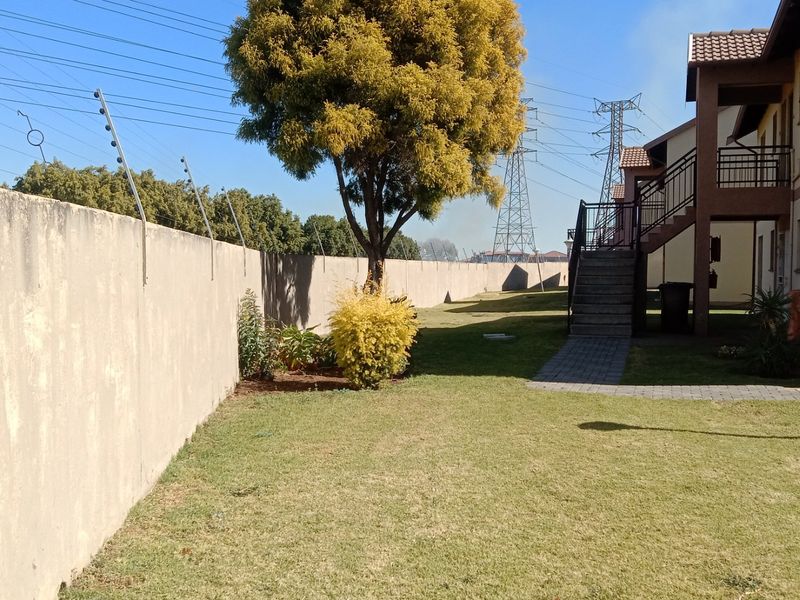 Rear exterior view of the apartment complex featuring a lawn, perimeter wall with electric fencing, and an external staircase leading to upper units.