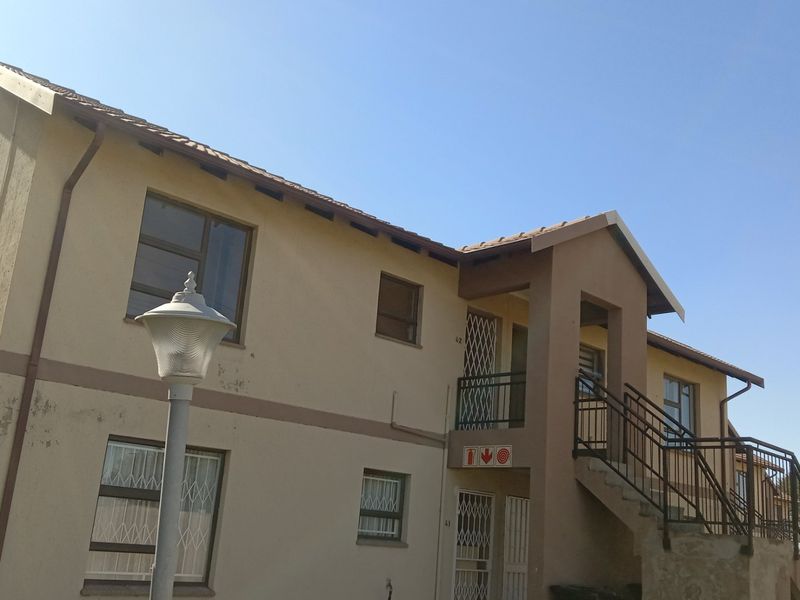 Exterior view of a multi-story apartment building featuring a tiled roof, external staircase with metal railings, and security gates on the entrance doors.
