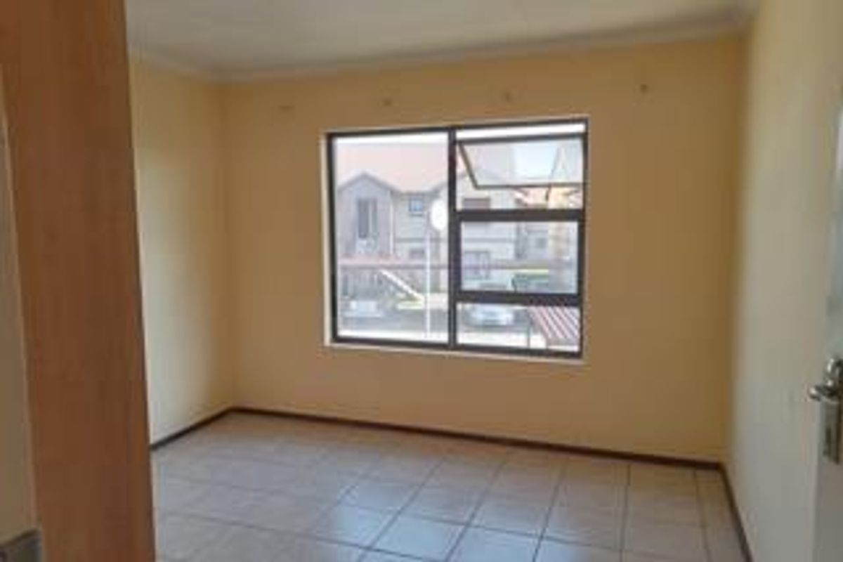 An empty bedroom featuring tiled flooring, neutral wall paint, and an aluminium window frame, offering a blank canvas for personalization.
