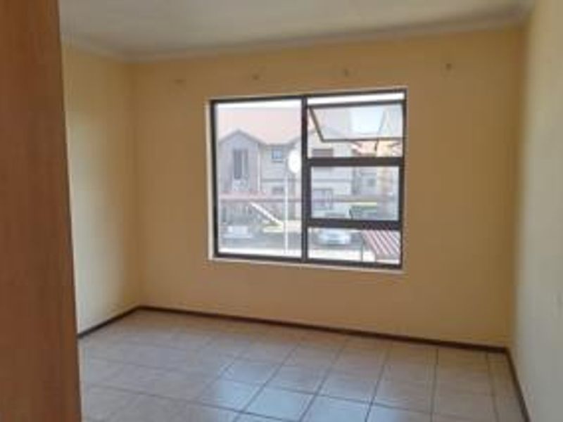 An empty bedroom featuring tiled flooring, neutral wall paint, and an aluminium window frame, offering a blank canvas for personalization.