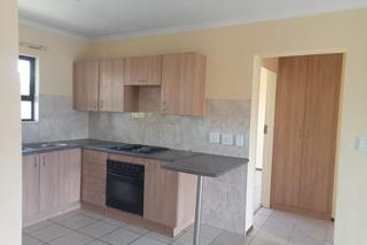 A functional kitchen featuring light wood-finish cabinetry, a built-in oven and hob, tiled backsplash, and a convenient breakfast bar, with adjacent built-in storage.