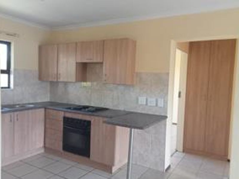 A functional kitchen featuring light wood-finish cabinetry, a built-in oven and hob, tiled backsplash, and a convenient breakfast bar, with adjacent built-in storage.