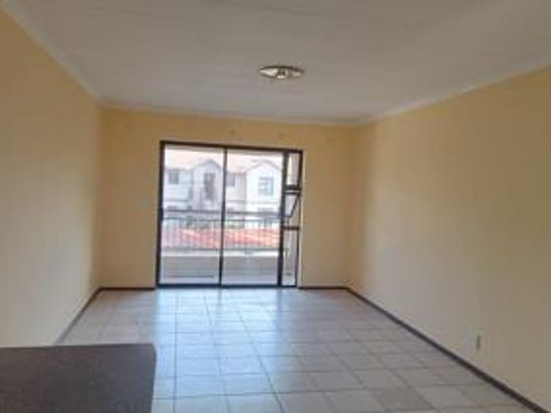 An empty, open-plan living area featuring tiled flooring, neutral walls, and a sliding glass door providing access to an outdoor balcony.