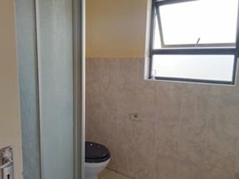 A functional bathroom featuring tiled walls, a standard toilet, and a top-hung window for ventilation.