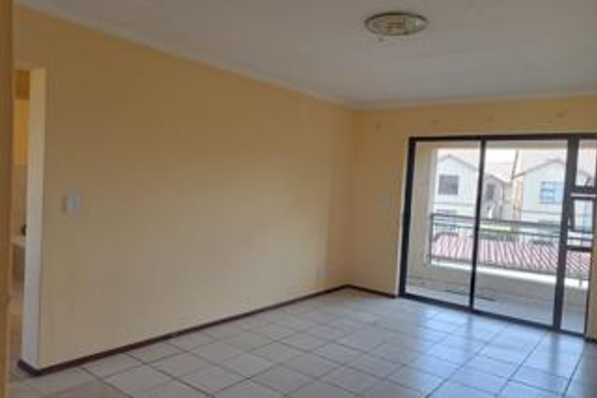 An empty, neutrally painted living room featuring tiled flooring and a large sliding glass door that provides access to an outdoor balcony.