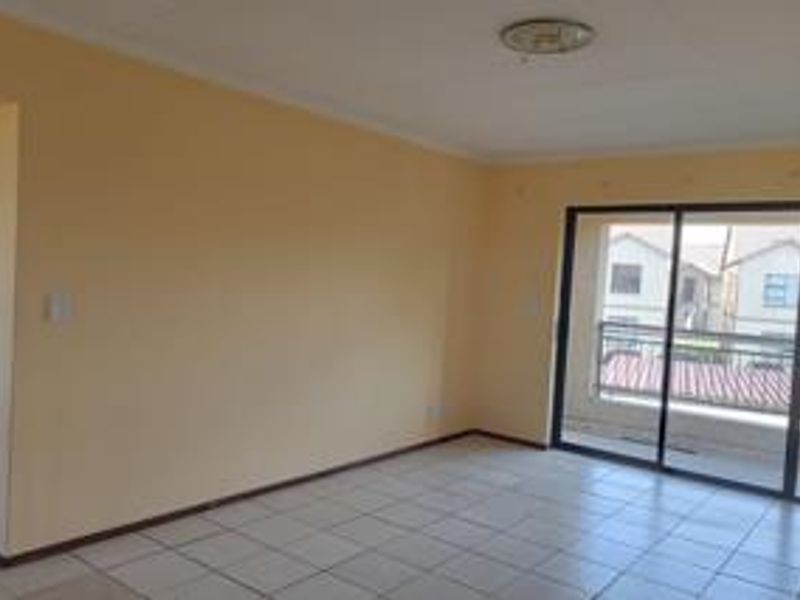 An empty, neutrally painted living room featuring tiled flooring and a large sliding glass door that provides access to an outdoor balcony.