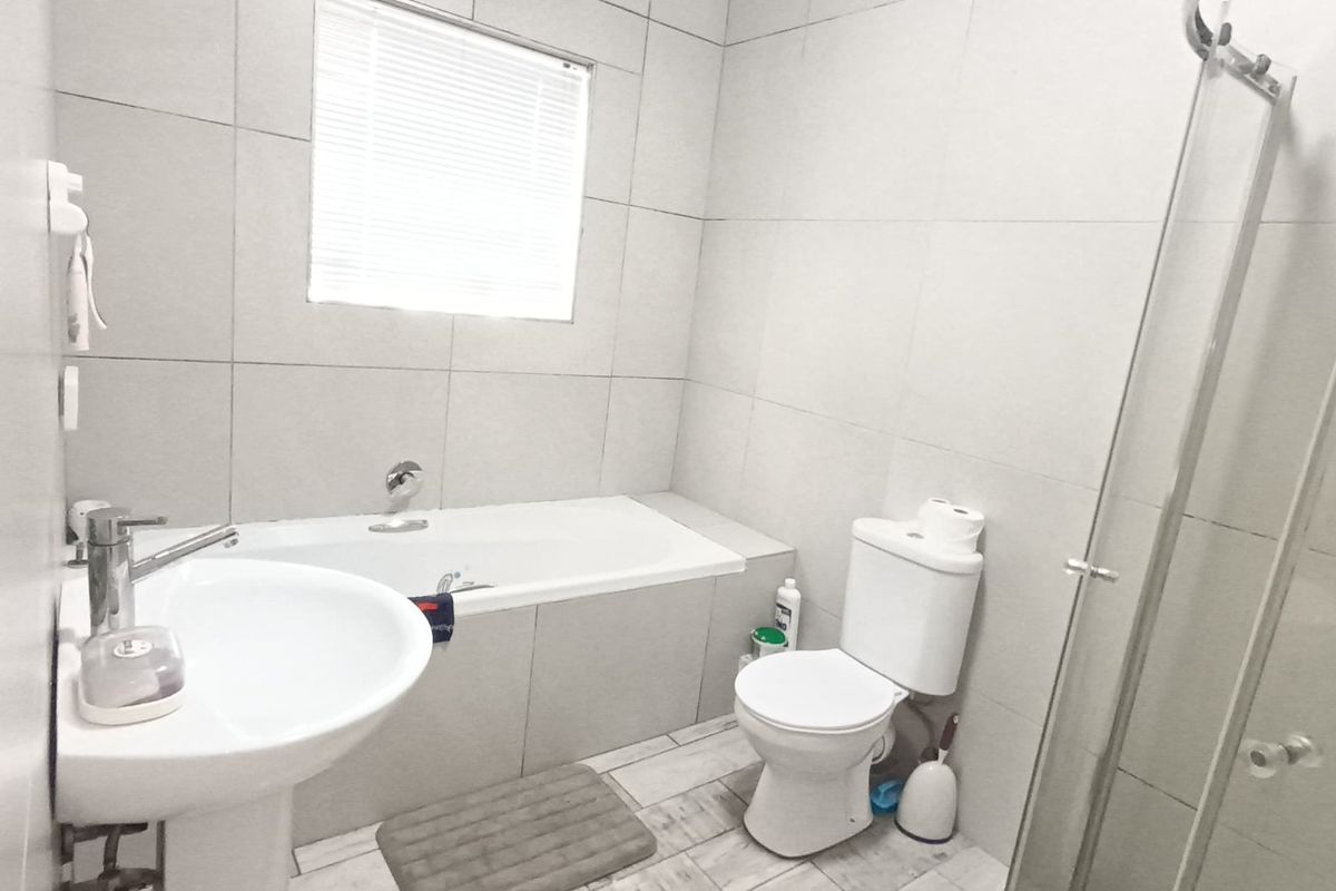A modern bathroom featuring a pedestal basin, built-in bathtub, toilet, and a separate glass-enclosed shower with neutral wall and floor tiling.