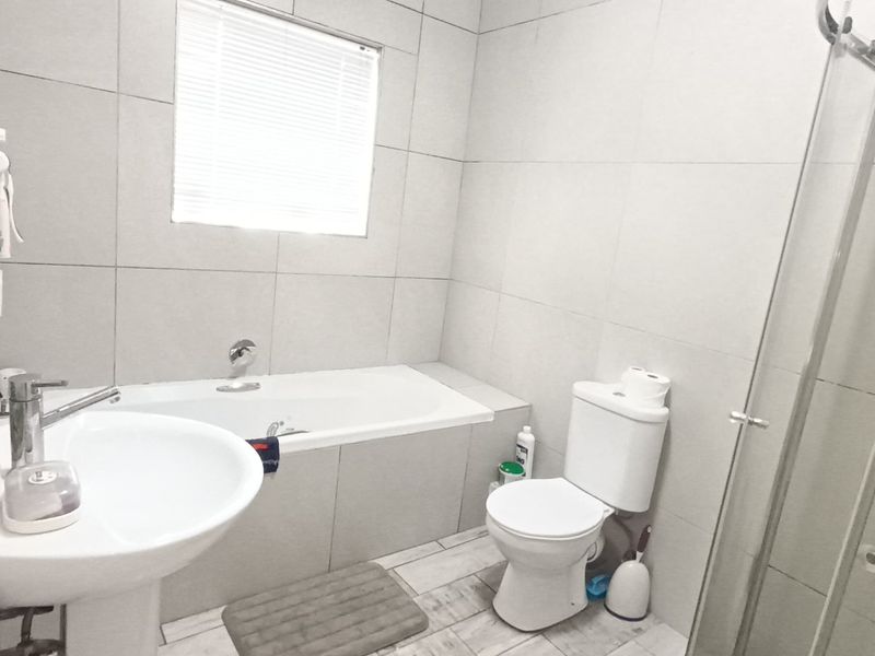A modern bathroom featuring a pedestal basin, built-in bathtub, toilet, and a separate glass-enclosed shower with neutral wall and floor tiling.