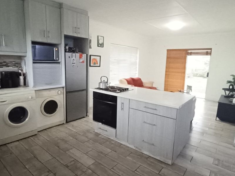 Open plan kitchen and living area featuring modern cabinetry, a central island with built-in oven and hob, and tiled flooring leading to a sliding door.
