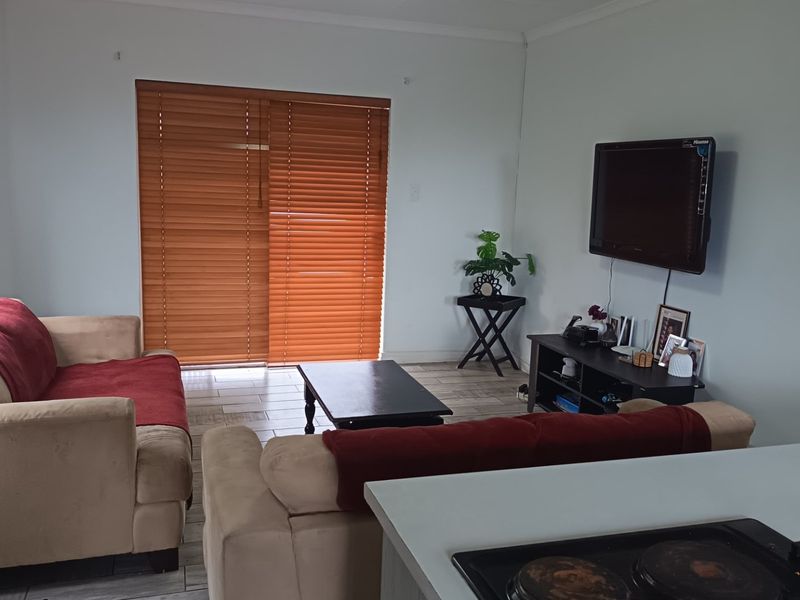 Open-plan living area featuring tiled flooring, venetian blinds, and a sliding door leading to the exterior, with an integrated kitchen hob visible.