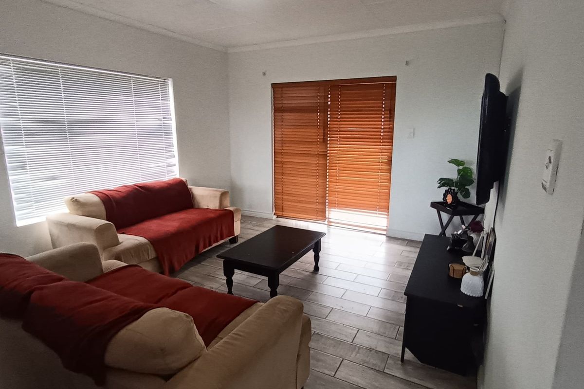 A bright living room featuring tiled flooring and a sliding glass door with wooden blinds, providing natural light and access to the outdoors.