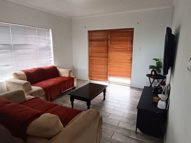 A bright living room featuring tiled flooring and a sliding glass door with wooden blinds, providing natural light and access to the outdoors.