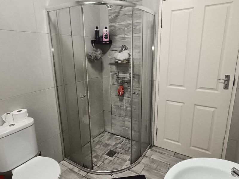 A functional bathroom featuring a corner shower enclosure, tiled walls and flooring, a pedestal basin, and a dual flush toilet.