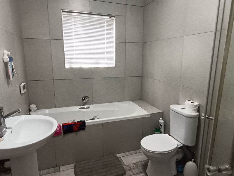 A functional bathroom featuring a pedestal basin, built-in bathtub, toilet, and a separate shower enclosure with neutral wall and floor tiling.