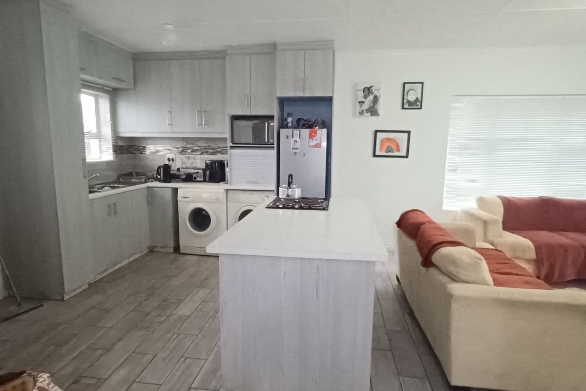Open-plan living area featuring a functional kitchen with built-in cabinetry, a central island with a hob, and tiled flooring throughout.