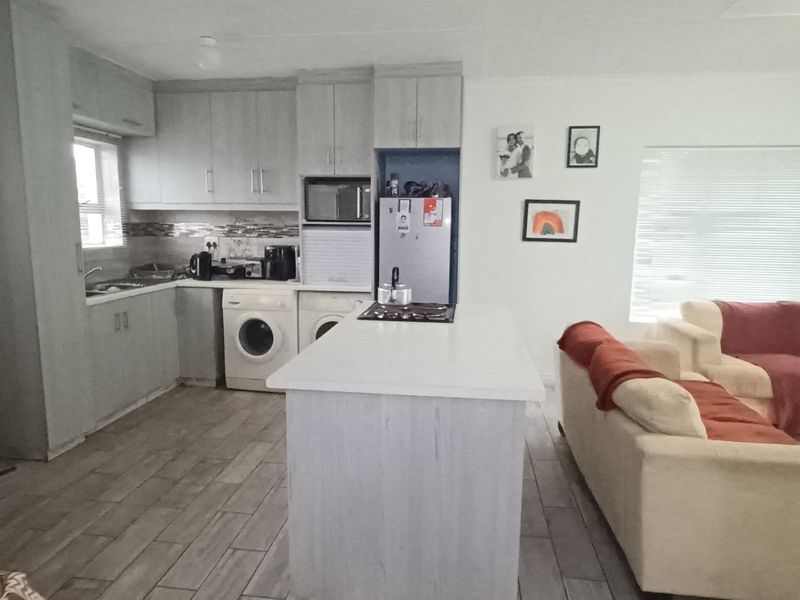 Open-plan living area featuring a functional kitchen with built-in cabinetry, a central island with a hob, and tiled flooring throughout.