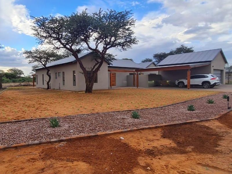 A modern single-story house featuring a metal roof, attached carport, and landscaped front yard with gravel pathways and established trees.