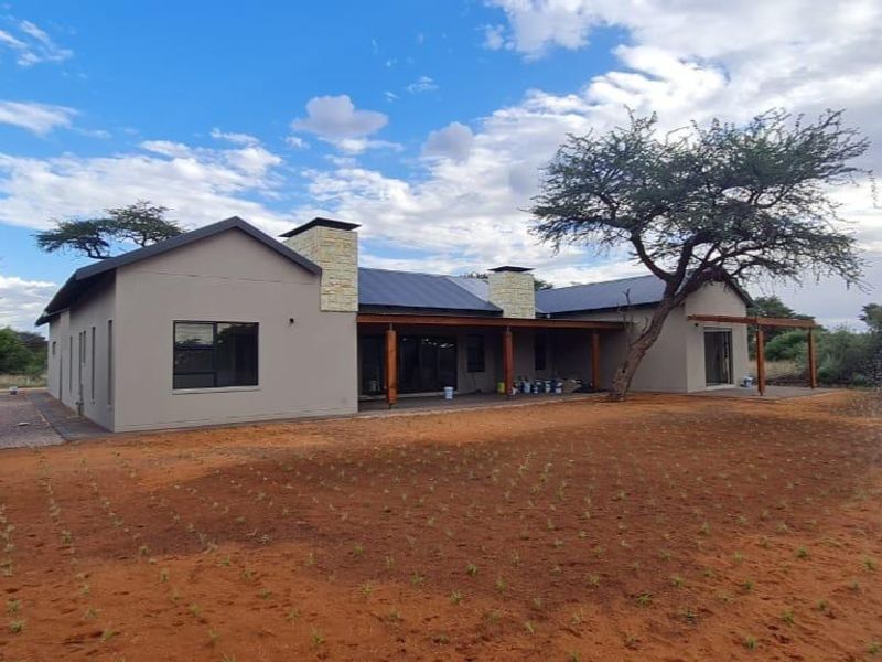Rear view of a modern single-story house featuring a covered patio, stone-clad chimneys, and large sliding glass doors set in a natural landscape.