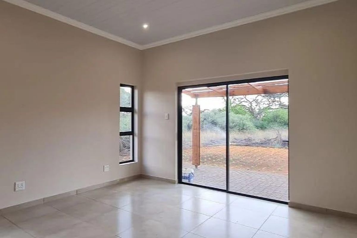 A bright, empty living room featuring tiled floors, recessed lighting, and a large sliding glass door providing access to an outdoor patio area.