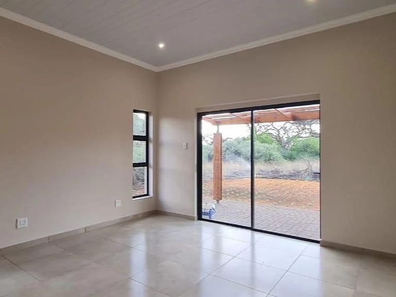A bright, empty living room featuring tiled floors, recessed lighting, and a large sliding glass door providing access to an outdoor patio area.
