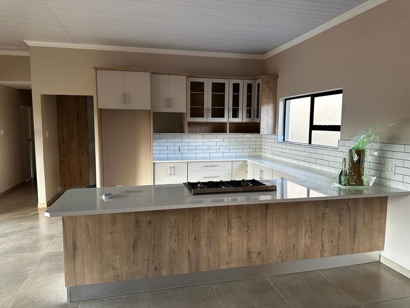 Modern kitchen featuring wood-look cabinetry, stone countertops, a central island with a gas hob, and a clean subway tile backsplash.