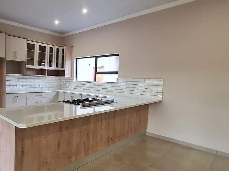 Modern kitchen featuring light wood-finish cabinetry, stone countertops, a gas hob, and a clean subway tile backsplash in a bright, open-plan layout.